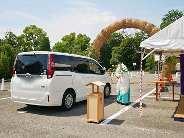 京都・城南宮の大茅の輪をくぐる前に宮司からお祓いを受けている白い車の画像。