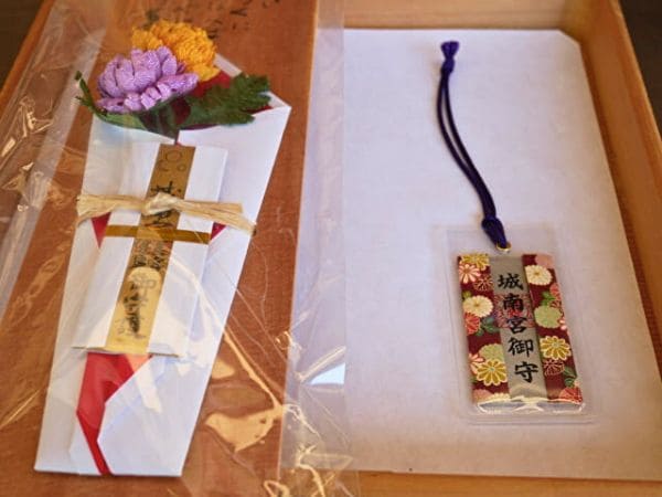 京都・城南宮の美容健康（うるわし）御札と菊の花守りの画像。御札には黄色と紫の菊の造花が添えられています。