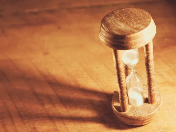 少し暗い光の中、長い影が伸びる傾いた砂時計の画像。