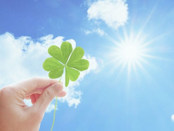 快晴の青空に四つ葉のクローバーをかざす画像。